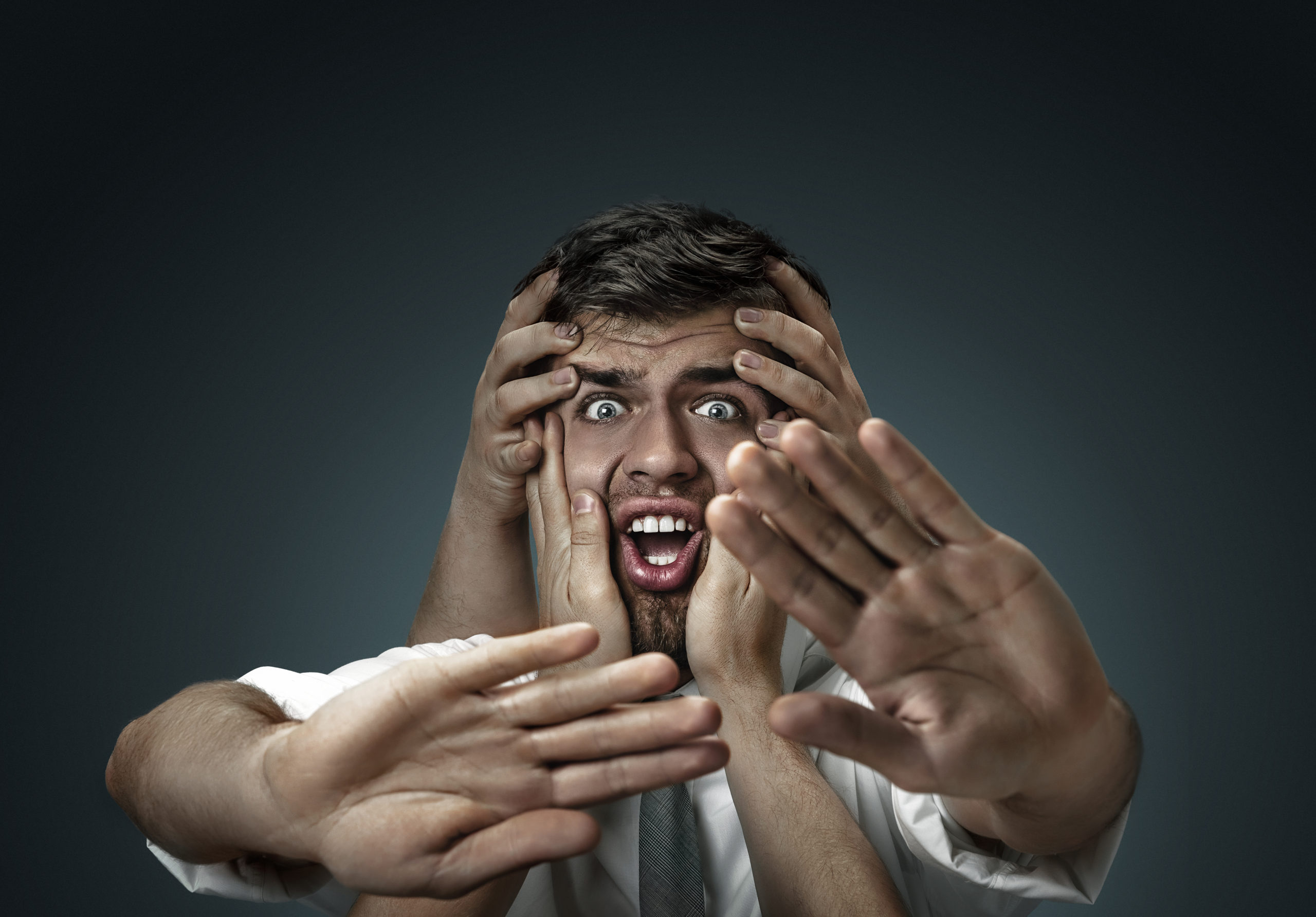 A male model surrounded by hands like his own thoughts on dark background. A young man doubts, can't choose the right decision and decide. Concept of mental problems, troubles in work, indecision.